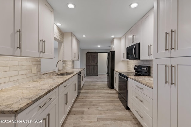 kitchen with a barn door, a sink, white cabinets, light stone countertops, and black appliances