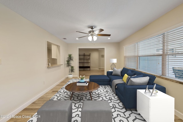 living room with visible vents, a ceiling fan, a textured ceiling, light wood-type flooring, and baseboards