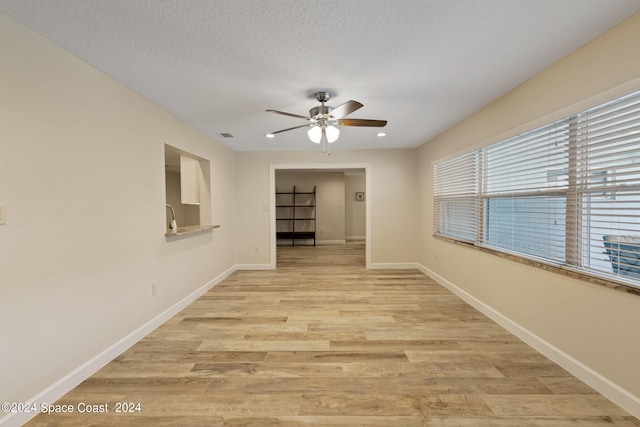 unfurnished room with a sink, ceiling fan, a textured ceiling, light wood-type flooring, and baseboards