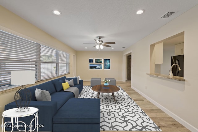 living room with visible vents, baseboards, light wood-style flooring, a textured ceiling, and recessed lighting