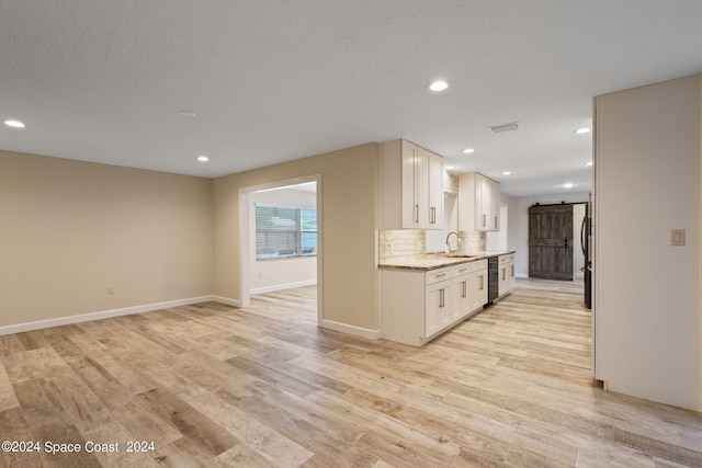 kitchen featuring a barn door, light stone counters, light wood-style floors, white cabinetry, and a sink