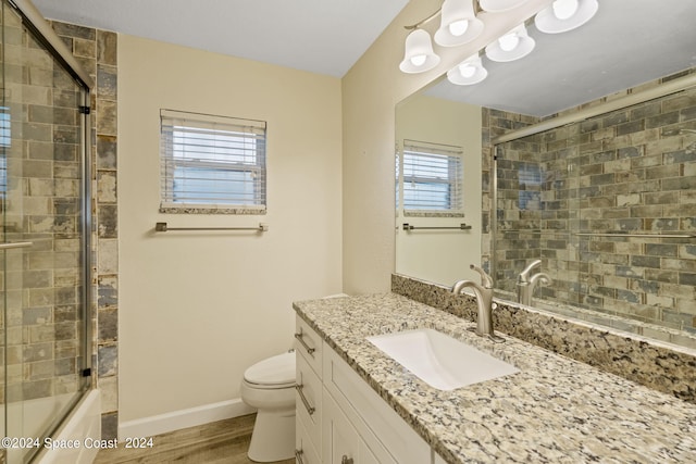 bathroom with toilet, bath / shower combo with glass door, wood finished floors, vanity, and baseboards