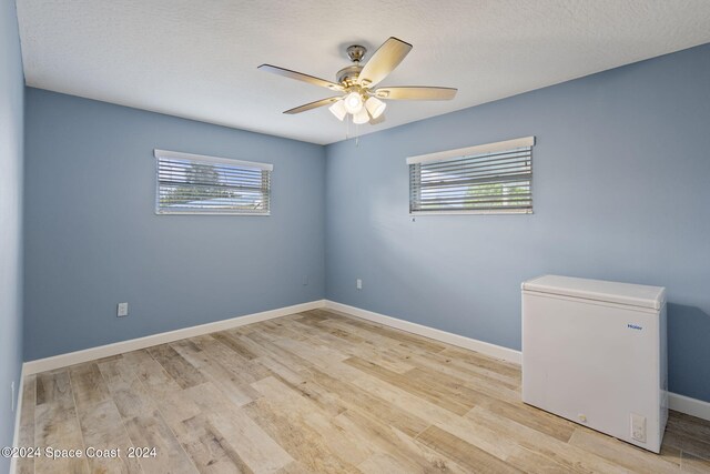 spare room featuring baseboards, a textured ceiling, a ceiling fan, and light wood-style floors