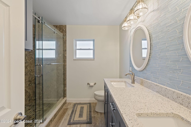 bathroom featuring toilet, wood finished floors, a sink, double vanity, and a stall shower