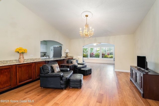 living area featuring a chandelier, arched walkways, light wood-style flooring, and baseboards