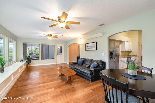 living room featuring light wood-style floors, arched walkways, visible vents, and a textured ceiling