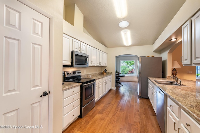 kitchen featuring appliances with stainless steel finishes, arched walkways, a sink, and light wood finished floors