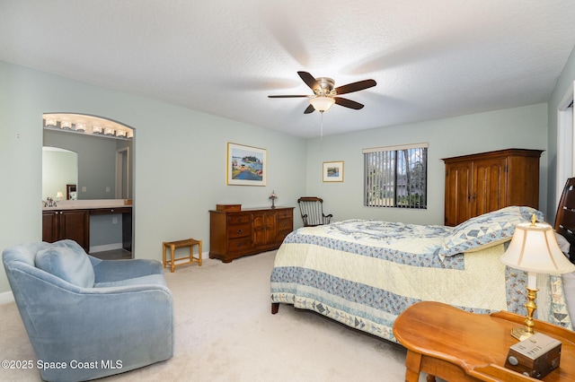 bedroom featuring arched walkways, ceiling fan, ensuite bathroom, a textured ceiling, and carpet floors