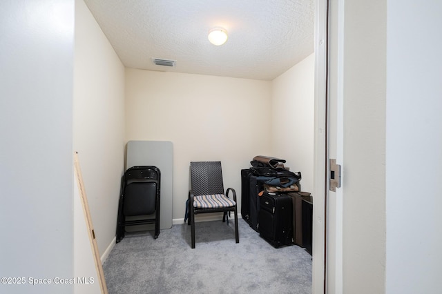 living area featuring a textured ceiling, carpet flooring, visible vents, and baseboards