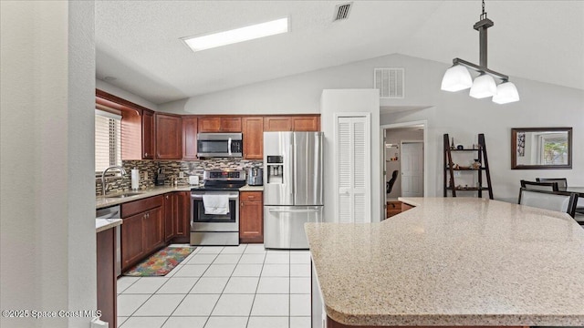 kitchen with appliances with stainless steel finishes, lofted ceiling, decorative backsplash, hanging light fixtures, and light stone countertops