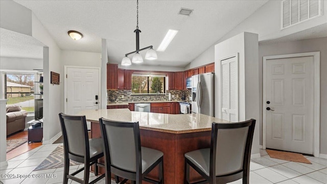 kitchen featuring light tile patterned flooring, appliances with stainless steel finishes, decorative light fixtures, lofted ceiling, and decorative backsplash