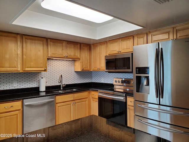 kitchen featuring appliances with stainless steel finishes, sink, backsplash, dark stone counters, and a raised ceiling