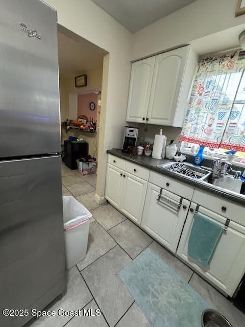 kitchen featuring light tile patterned flooring, white cabinets, sink, and stainless steel refrigerator