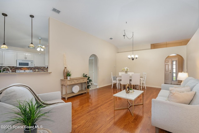 living room with wood-type flooring, lofted ceiling, sink, and ceiling fan with notable chandelier