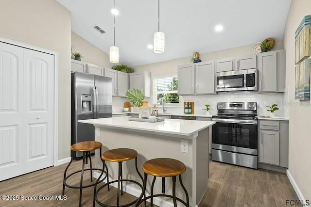 kitchen with a center island, stainless steel appliances, decorative light fixtures, and gray cabinets