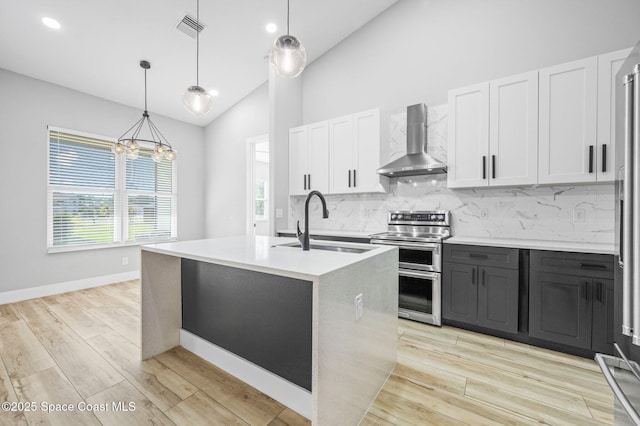 kitchen with wall chimney exhaust hood, decorative light fixtures, white cabinets, sink, and range with two ovens