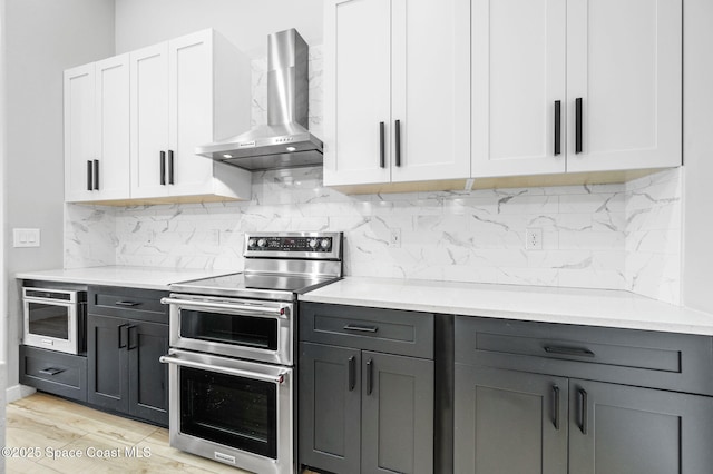 kitchen with wall chimney range hood, double oven range, white cabinetry, and tasteful backsplash