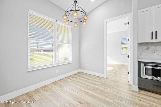 unfurnished dining area featuring a notable chandelier, heating unit, light wood-type flooring, and lofted ceiling