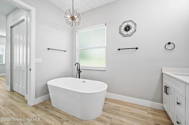 bathroom with wood-type flooring, a chandelier, a tub to relax in, and vanity