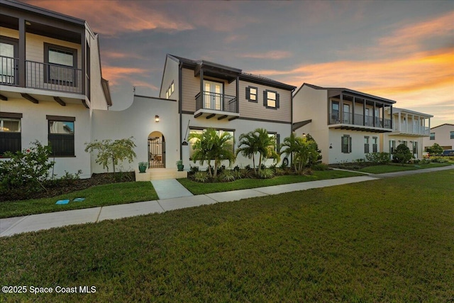 view of property featuring a front lawn, a balcony, and stucco siding