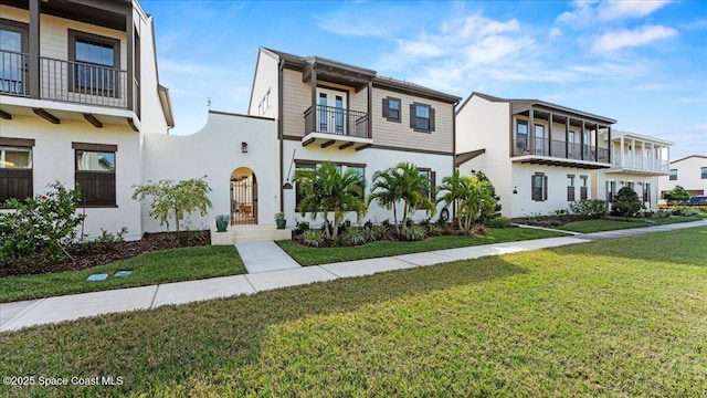 view of property with a front yard, a balcony, and stucco siding