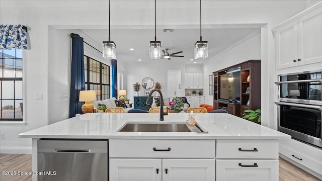 kitchen with light wood finished floors, open floor plan, stainless steel appliances, crown molding, and a sink