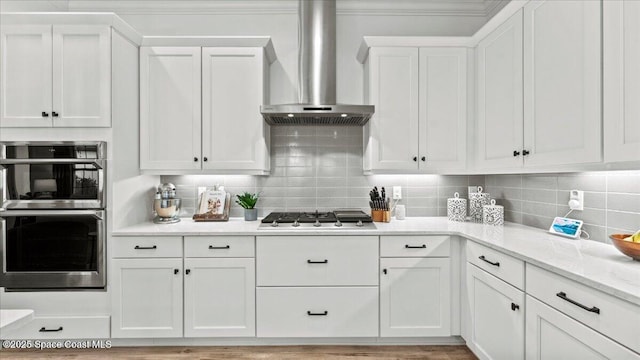 kitchen featuring white cabinets, backsplash, light stone counters, stainless steel appliances, and wall chimney exhaust hood