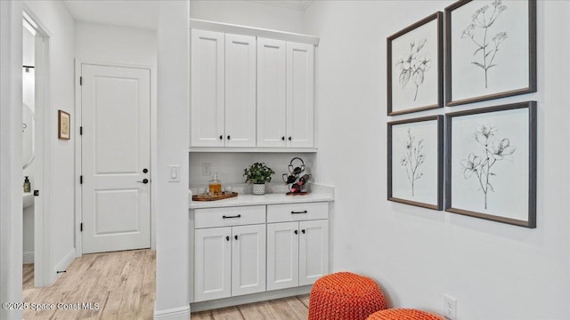 bar with white cabinets and light hardwood / wood-style flooring