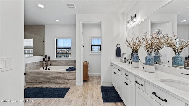 bathroom with double vanity, a garden tub, a sink, and wood finished floors