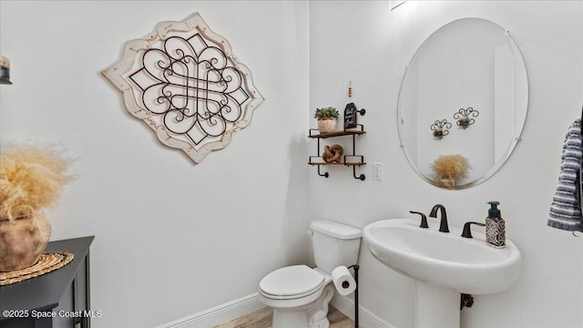 half bath featuring toilet, baseboards, and a sink