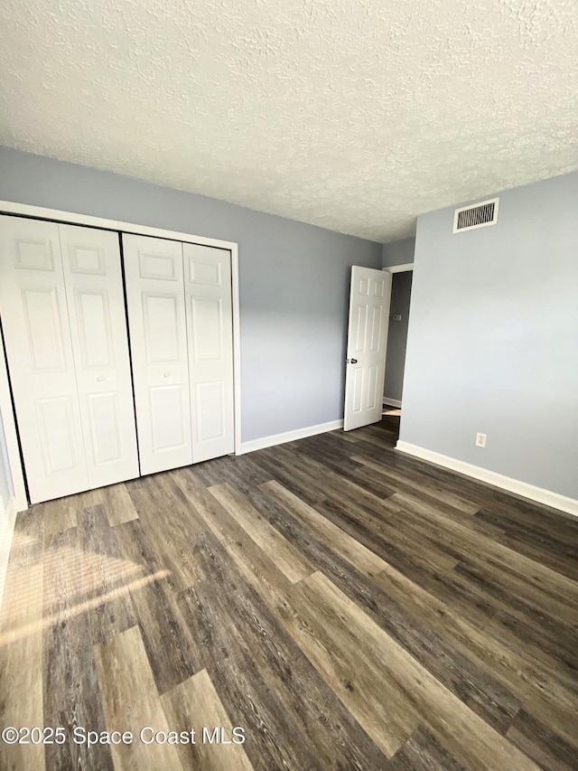 unfurnished bedroom featuring dark hardwood / wood-style flooring, a textured ceiling, and a closet