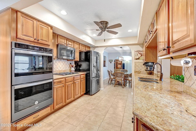 kitchen with appliances with stainless steel finishes, sink, backsplash, ceiling fan, and light stone counters