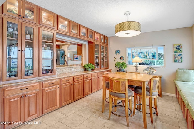 interior space with light tile patterned flooring, a kitchen bar, decorative light fixtures, a textured ceiling, and light stone countertops