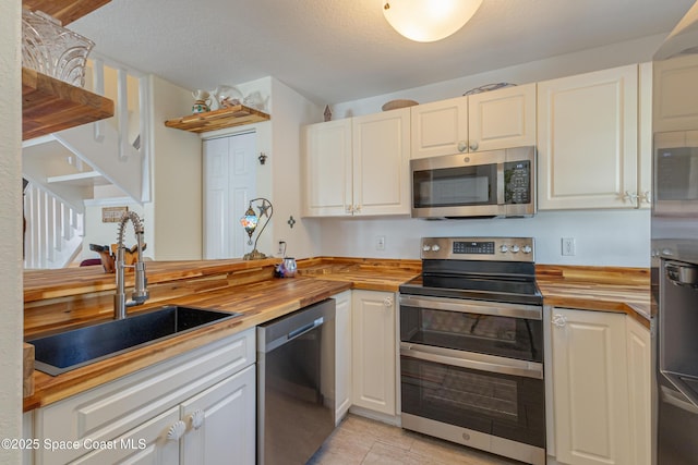 kitchen featuring sink, butcher block countertops, light tile patterned floors, stainless steel appliances, and white cabinets