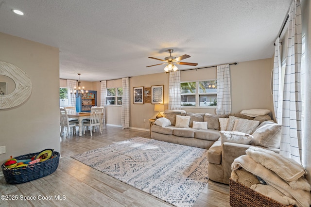 living room with a textured ceiling, ceiling fan with notable chandelier, light wood-style flooring, and baseboards