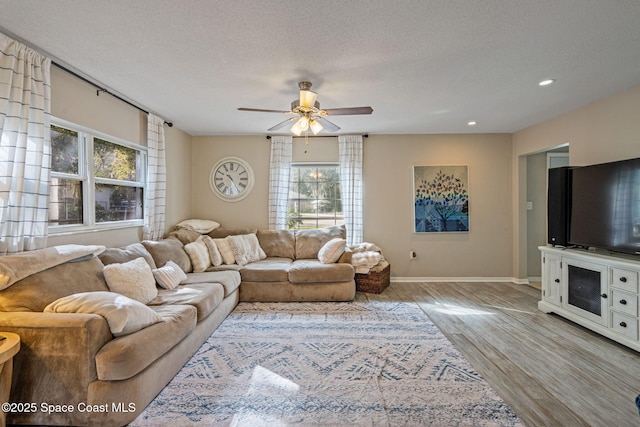 living room featuring baseboards, a ceiling fan, light wood-style flooring, a textured ceiling, and recessed lighting