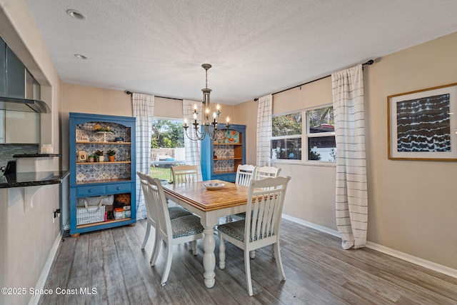 dining room with a chandelier, a textured ceiling, wood finished floors, and baseboards