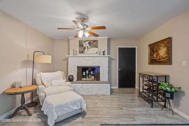 sitting room featuring ceiling fan, a stone fireplace, wood finished floors, and baseboards