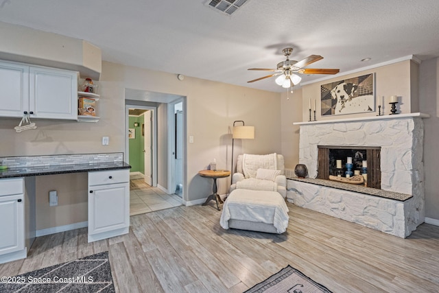 living area with visible vents, baseboards, a ceiling fan, light wood-style flooring, and a stone fireplace