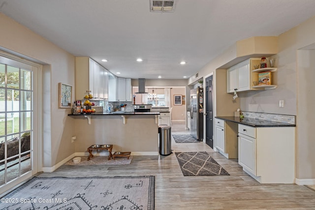 kitchen with visible vents, freestanding refrigerator, white cabinetry, wall chimney range hood, and a peninsula