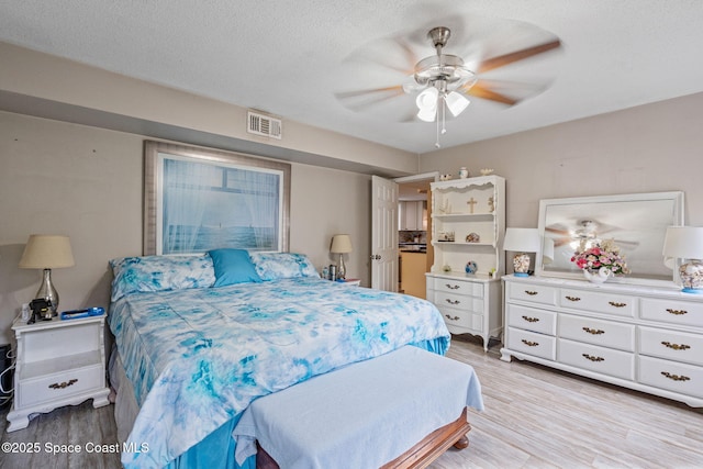 bedroom with light wood-style flooring, visible vents, ceiling fan, and a textured ceiling