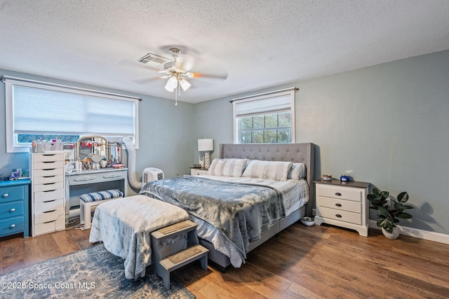 bedroom featuring dark wood-style floors, ceiling fan, visible vents, and a textured ceiling