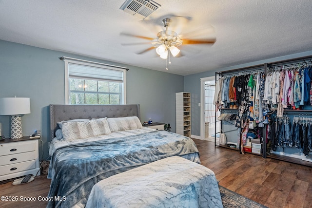 bedroom with ceiling fan, a textured ceiling, visible vents, and dark wood-type flooring