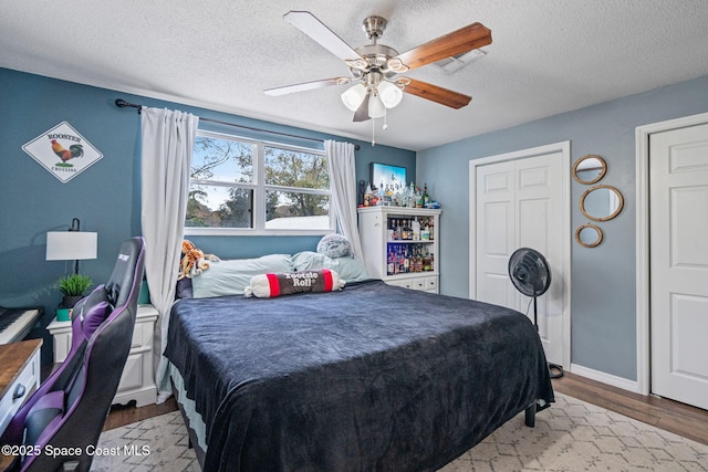 bedroom featuring baseboards, light wood-style flooring, a ceiling fan, and a textured ceiling