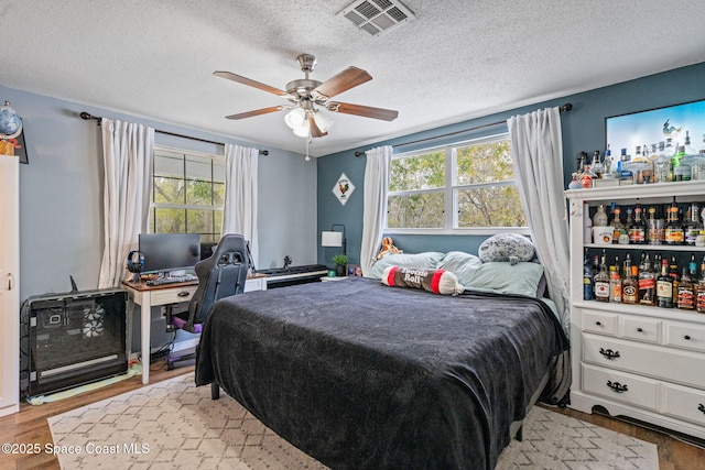 bedroom with a ceiling fan, light wood-type flooring, visible vents, and a textured ceiling