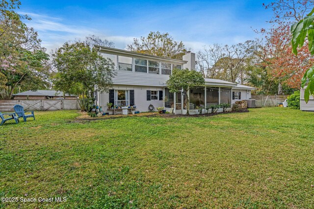 back of house featuring a sunroom, a fenced backyard, a chimney, and a yard