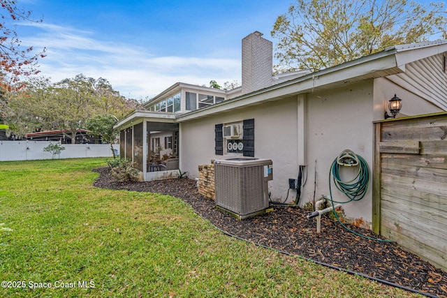 rear view of house featuring central AC unit, a fenced backyard, a sunroom, a lawn, and stucco siding