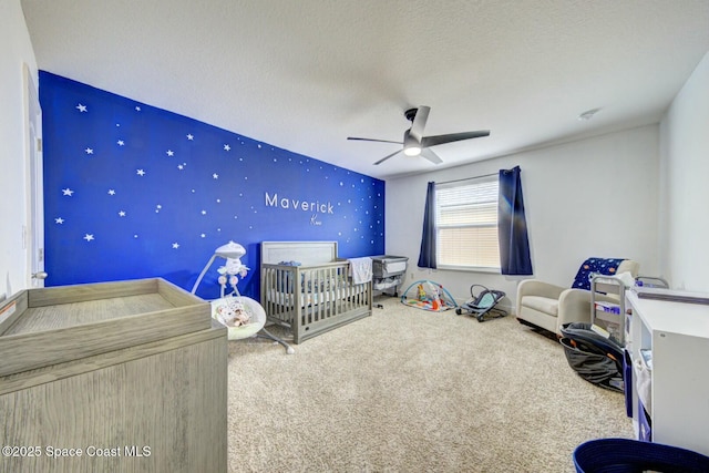 unfurnished bedroom with a textured ceiling, carpet floors, a nursery area, and ceiling fan