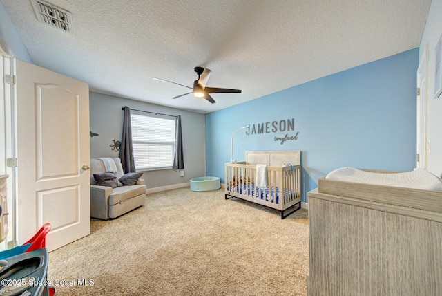 bedroom featuring a nursery area, light colored carpet, a textured ceiling, and ceiling fan