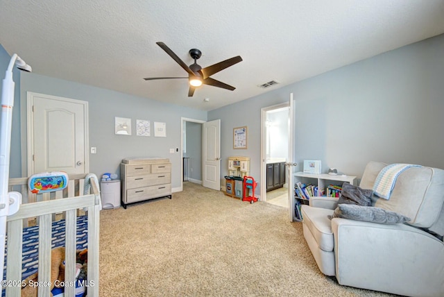 bedroom with ensuite bath, a crib, ceiling fan, a textured ceiling, and light colored carpet